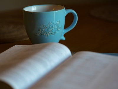 浅焦点摄影开放书旁边的蓝色的陶瓷杯
